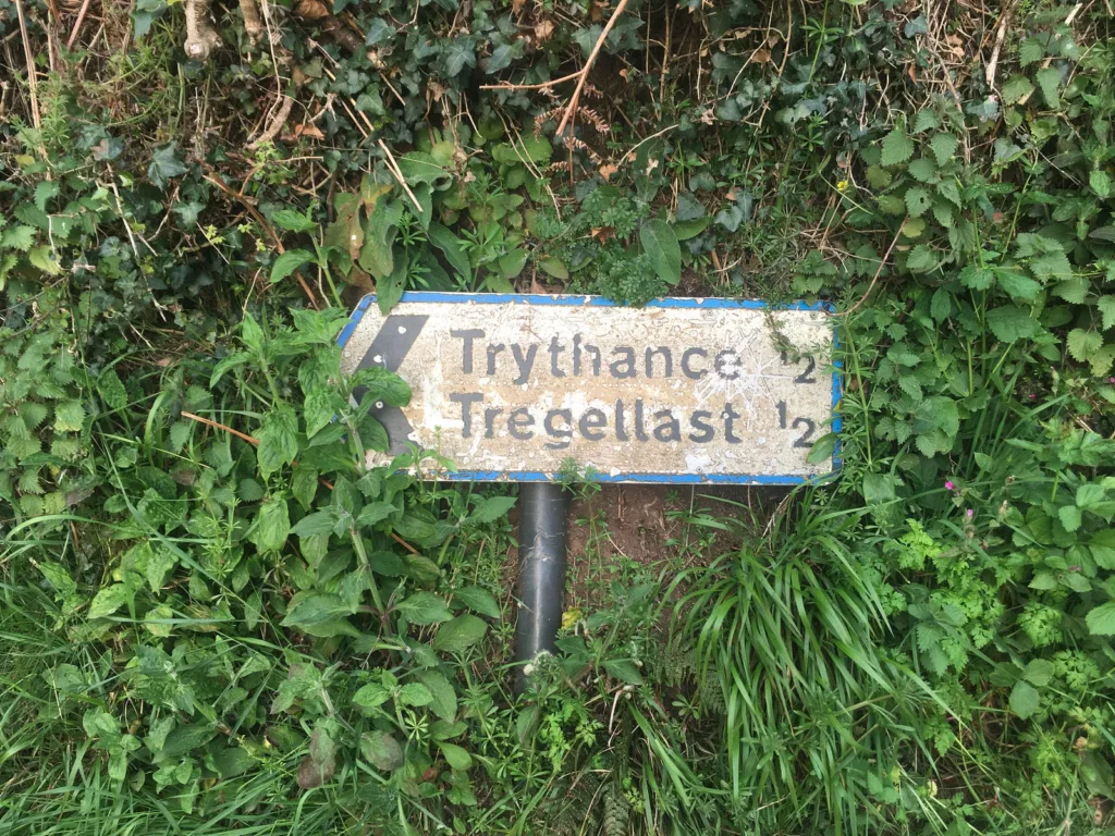 A sign to Trythance and Tregellast set against greenery.