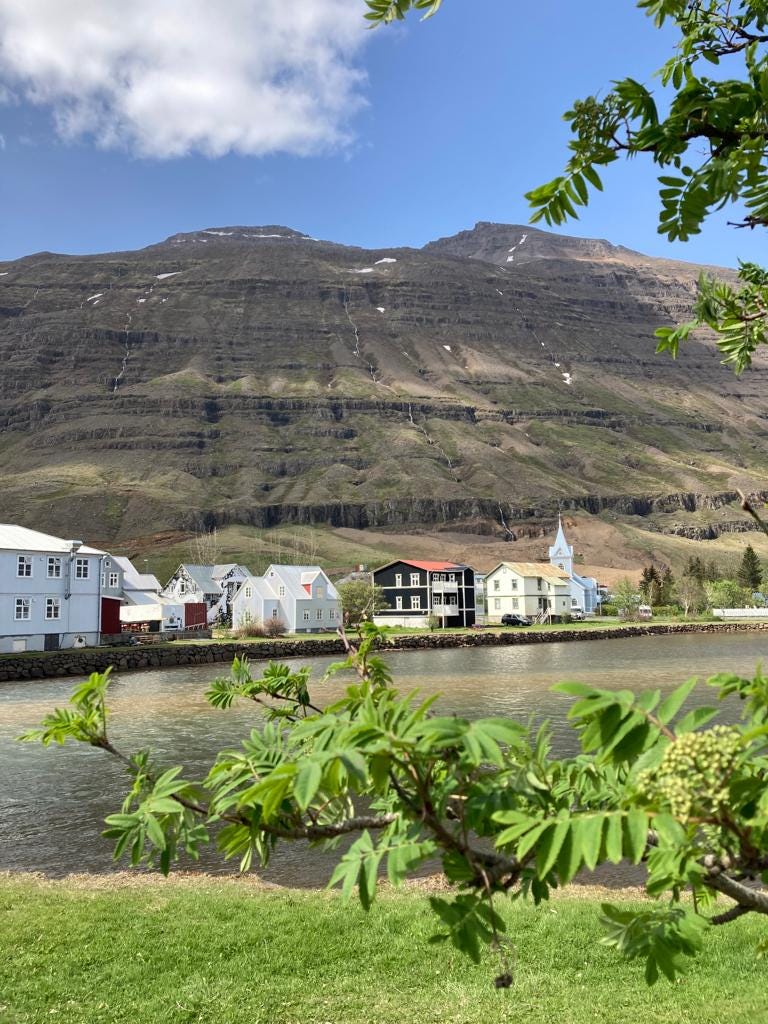Loch with wooden houses and steep brown mountains in the background.