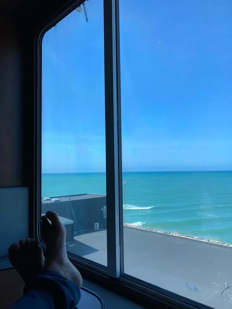 Feet put up on table overlooking window overlooking the sea.