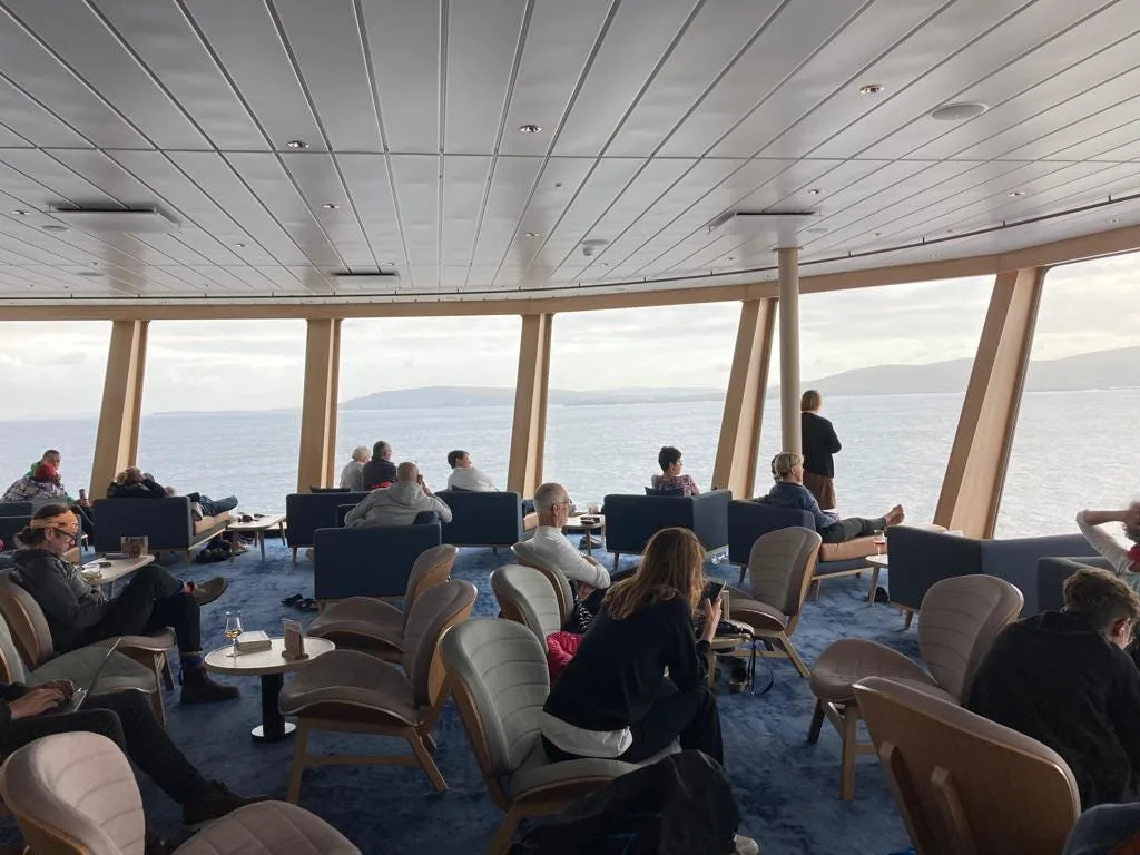 People sitting and standing on chairs overlooking the sea and Shetland Islands in the distance.