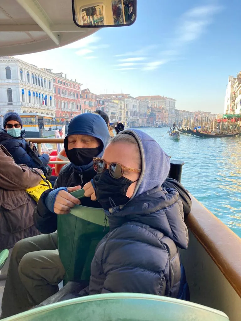 People on boat in Venice in jackets, sunglasses and masks.