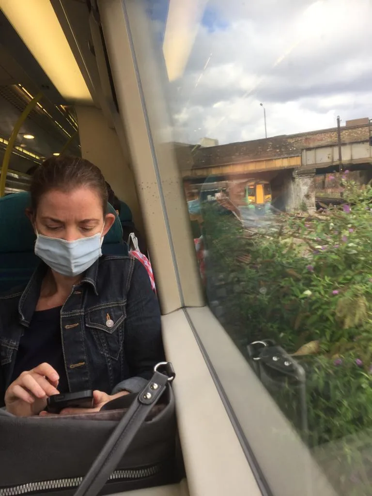 Rose sitting on train looking at her phone. Has a bag with her sensory kit in it.