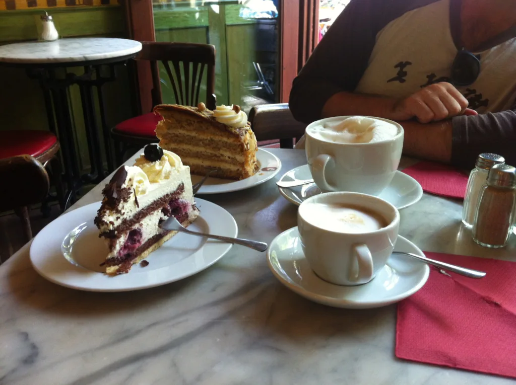 Two lattes on a table with a large slice of cake.