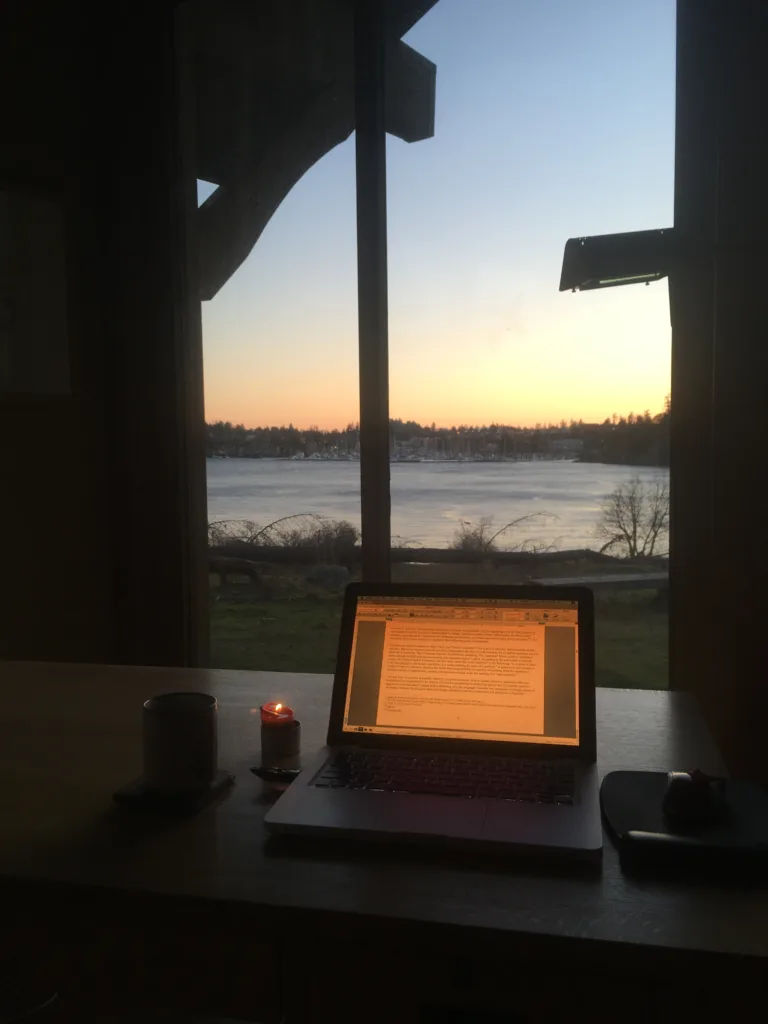 Dimmed laptop screen with a candle looking out the window at the sea in twilight.