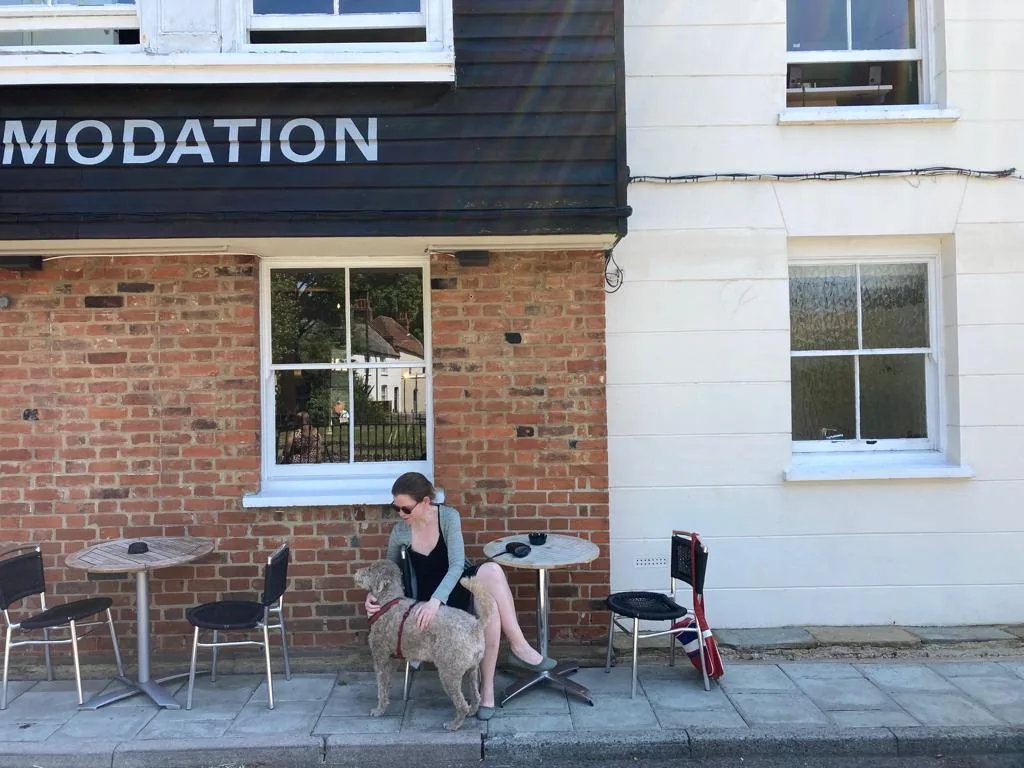 Woman in dress sitting with dog at an outside cafe.