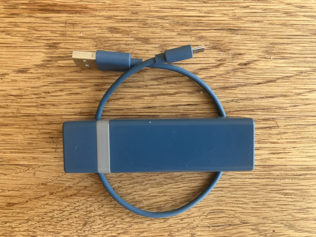 Blue battery charger for phone with blue cord on a wood floor.