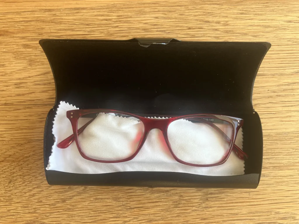 Red glasses inside a black carrying case on a wood floor.