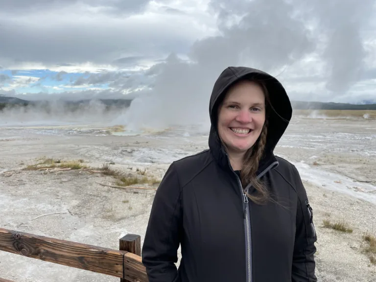 Jackie standing in black zipped hoodie in front of geyser.
