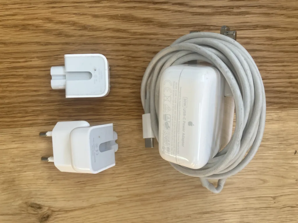 Macbook charger and two converters on a wood floor.