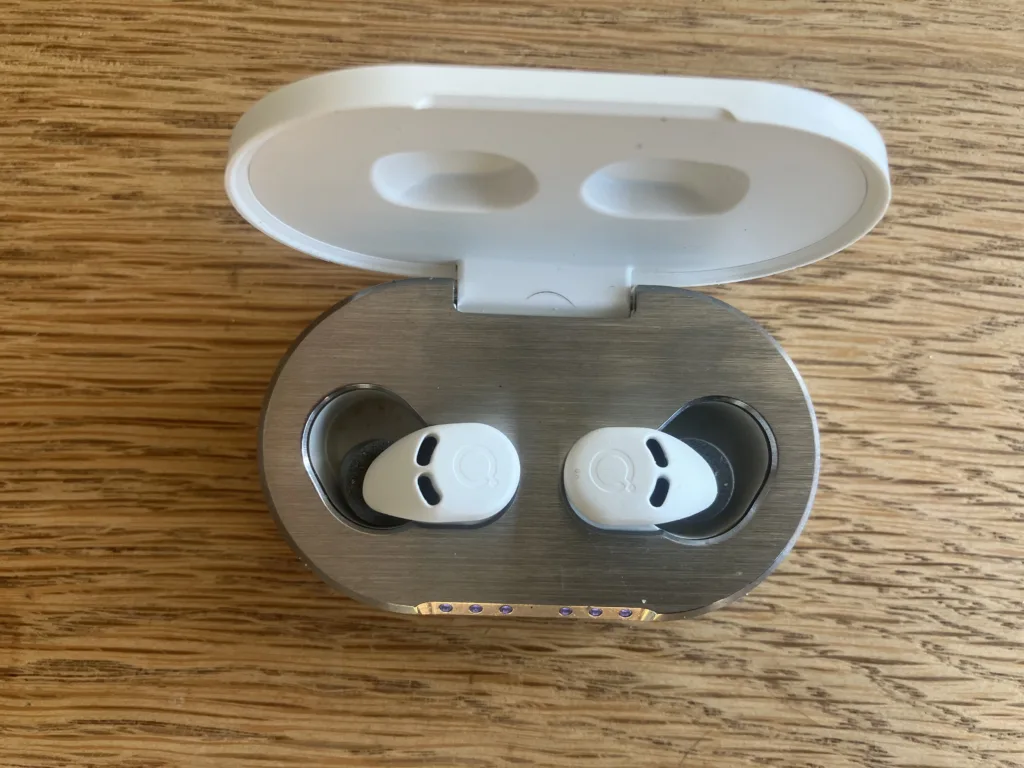 Open white box with two earbuds sitting on a wood floor.