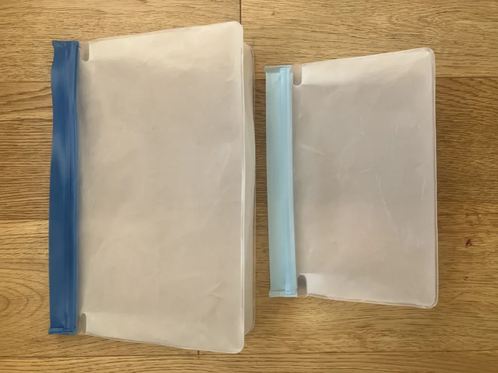 Two white and blue reusable ziplock bags on a wood floor.
