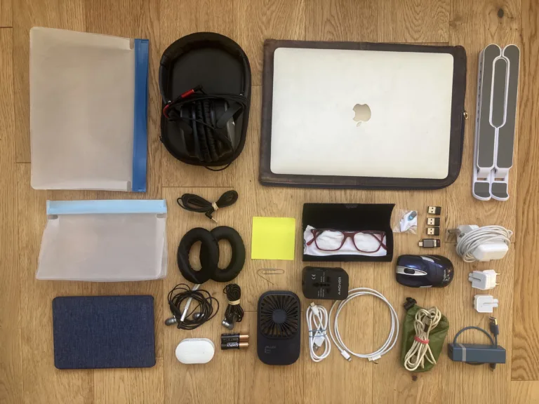 Essential Tech gear for digital nomads arranged on wood floor. Many electrical gadgets including a laptop and headphones.