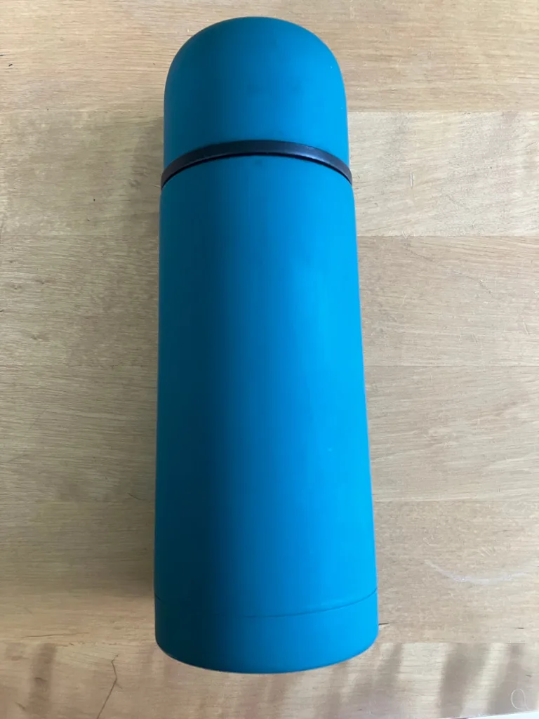 Blue and black thermos on wooden table.