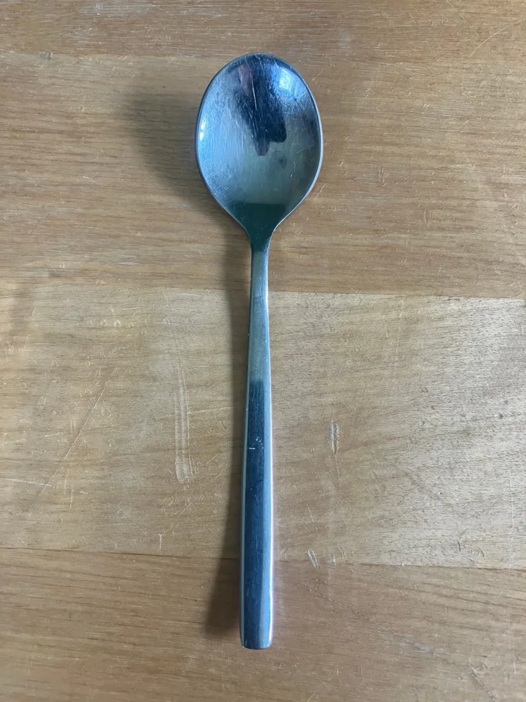 Tiny silver spoon on wooden table.