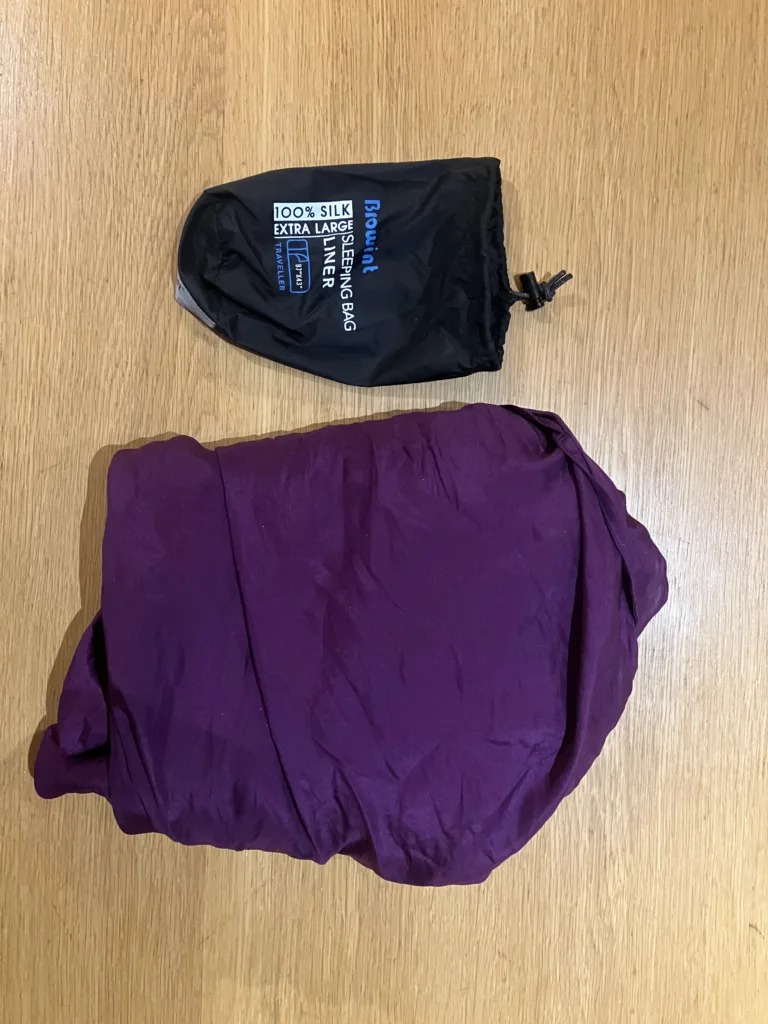 Purple sleep sack folded next to small black bag on wood table.