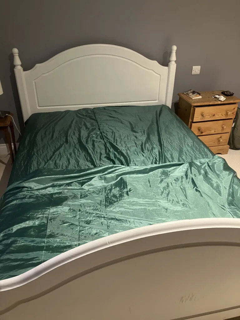 Green satin silk sheets covering bed with white bedframe next two two nightstands.