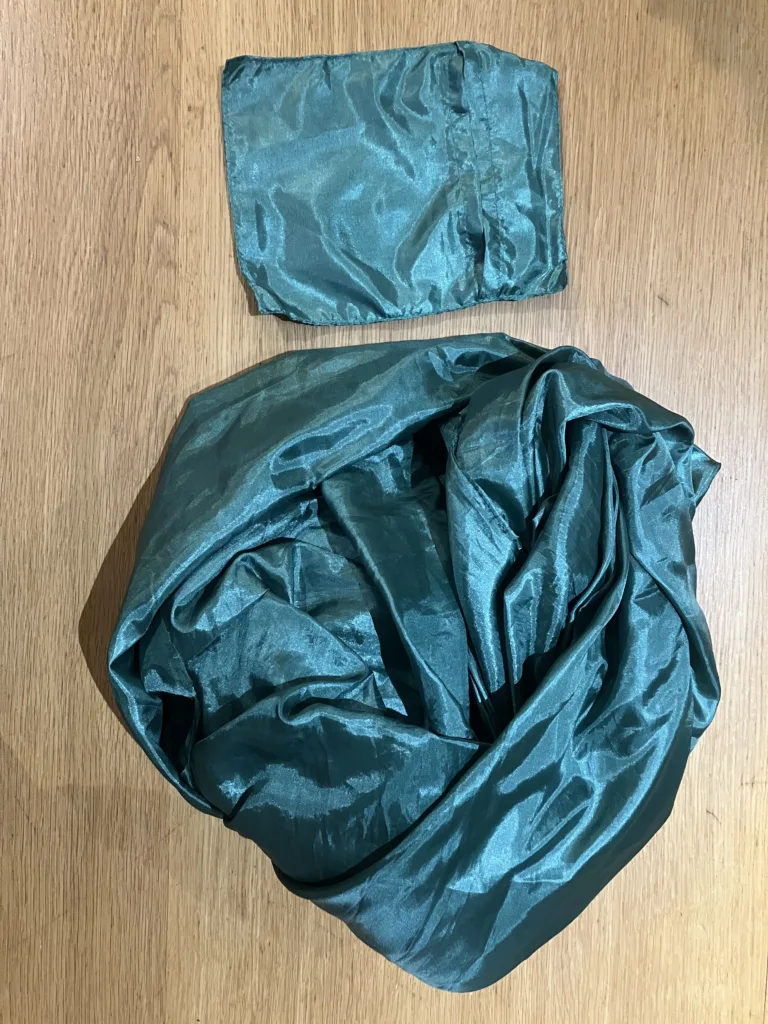 Folded green satin sleep sack next to green small bag on wooden table.