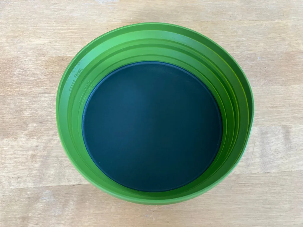 Green and gray opened silicone bowl on wooden table.
