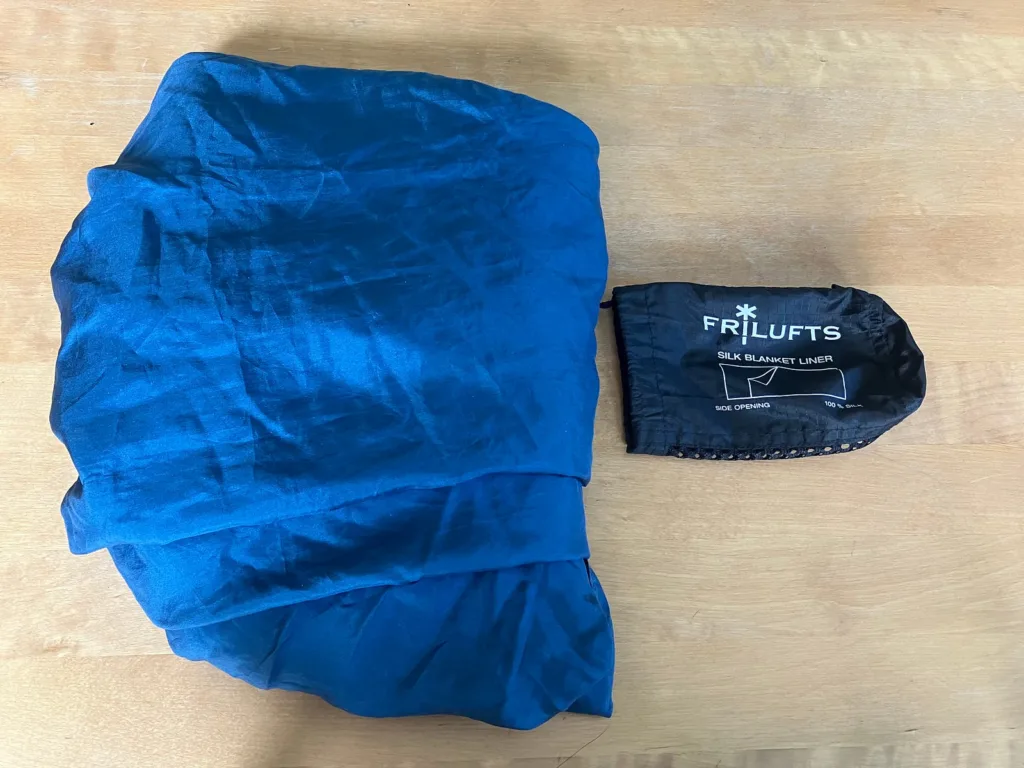 Blue silk sleep sack folded next to small black bag on wood table.