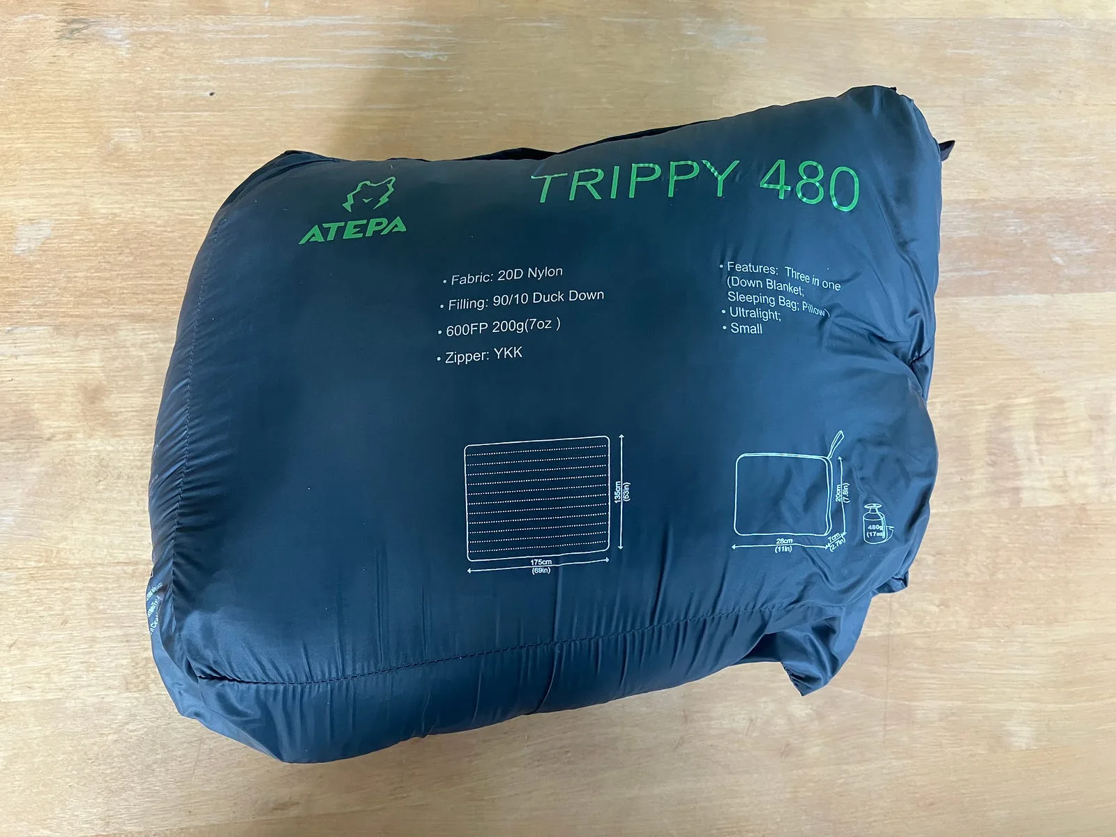 Rectangular gray stuffed sack with camping blanket on wooden table.