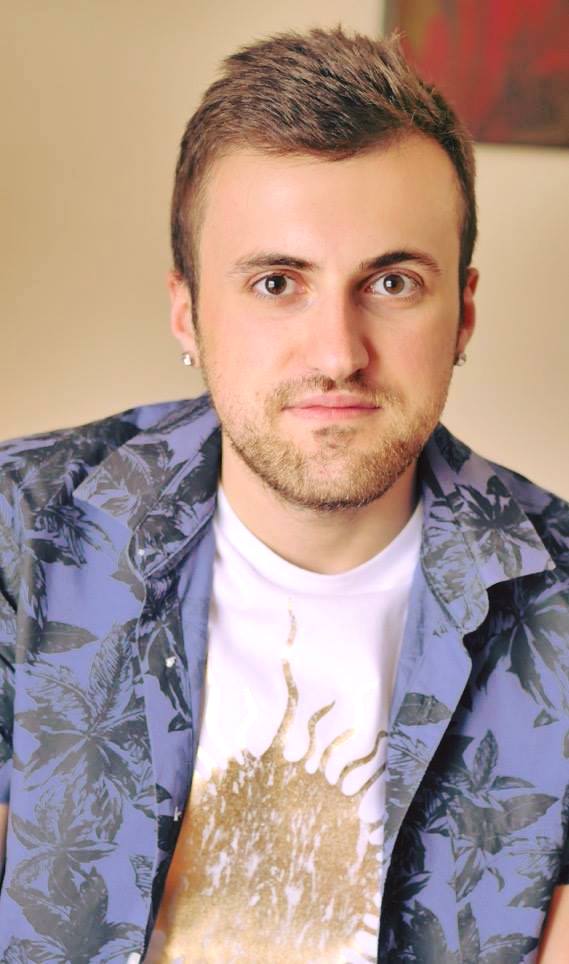 closeup of man with white t shirt and gold sun. Blue/black shirt over it and brown background.